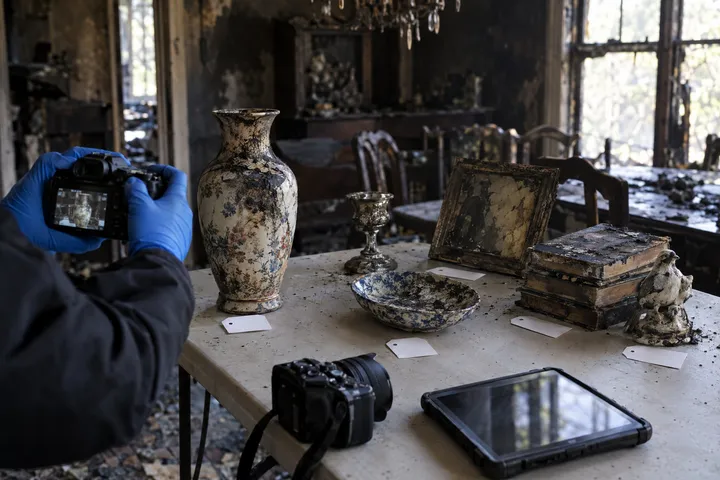Gloved hands photographing a sooty vase beside numbered inventory tags