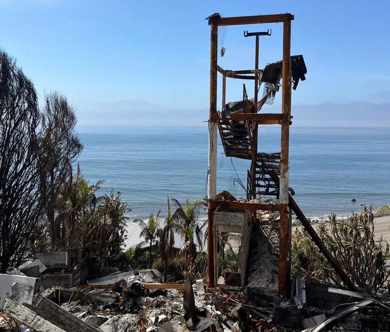 Fire-damaged coastal home reduced to its frame and rubble, field photograph.