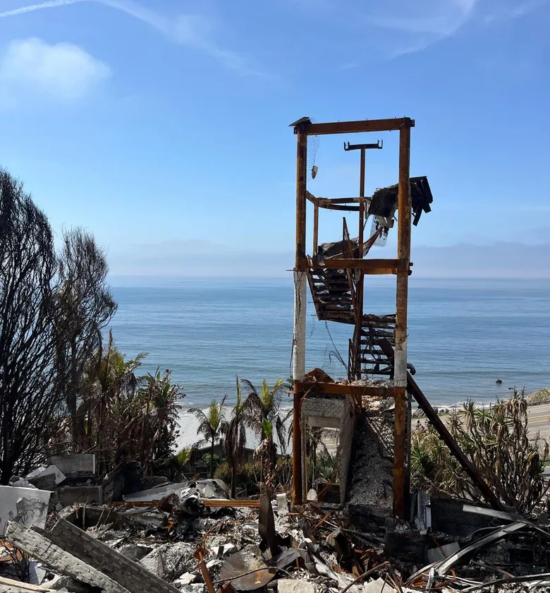 Burned stair frame of a hillside home above the ocean after a wildfire.