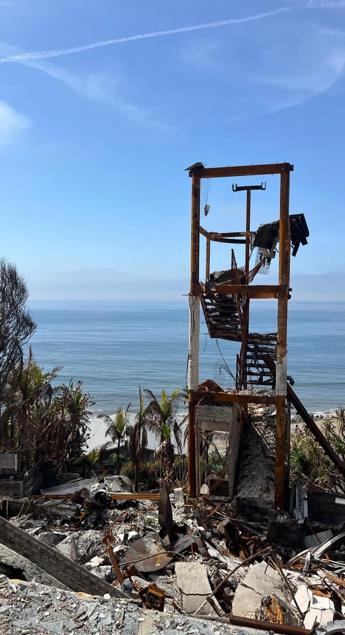 Burned stair frame of a hillside home above the ocean after a wildfire.