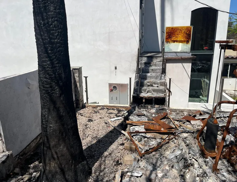 Fire-damaged exterior stair and debris beside a white house after a loss.