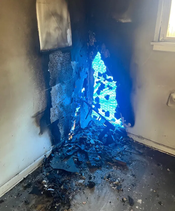 Smoke-blackened interior corner with a burned wall and debris on the floor.