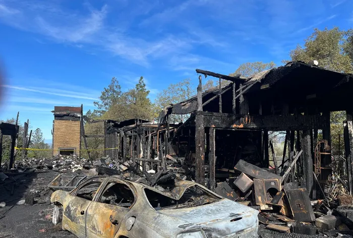 Burned wood-frame house and a burned-out car after a fire.